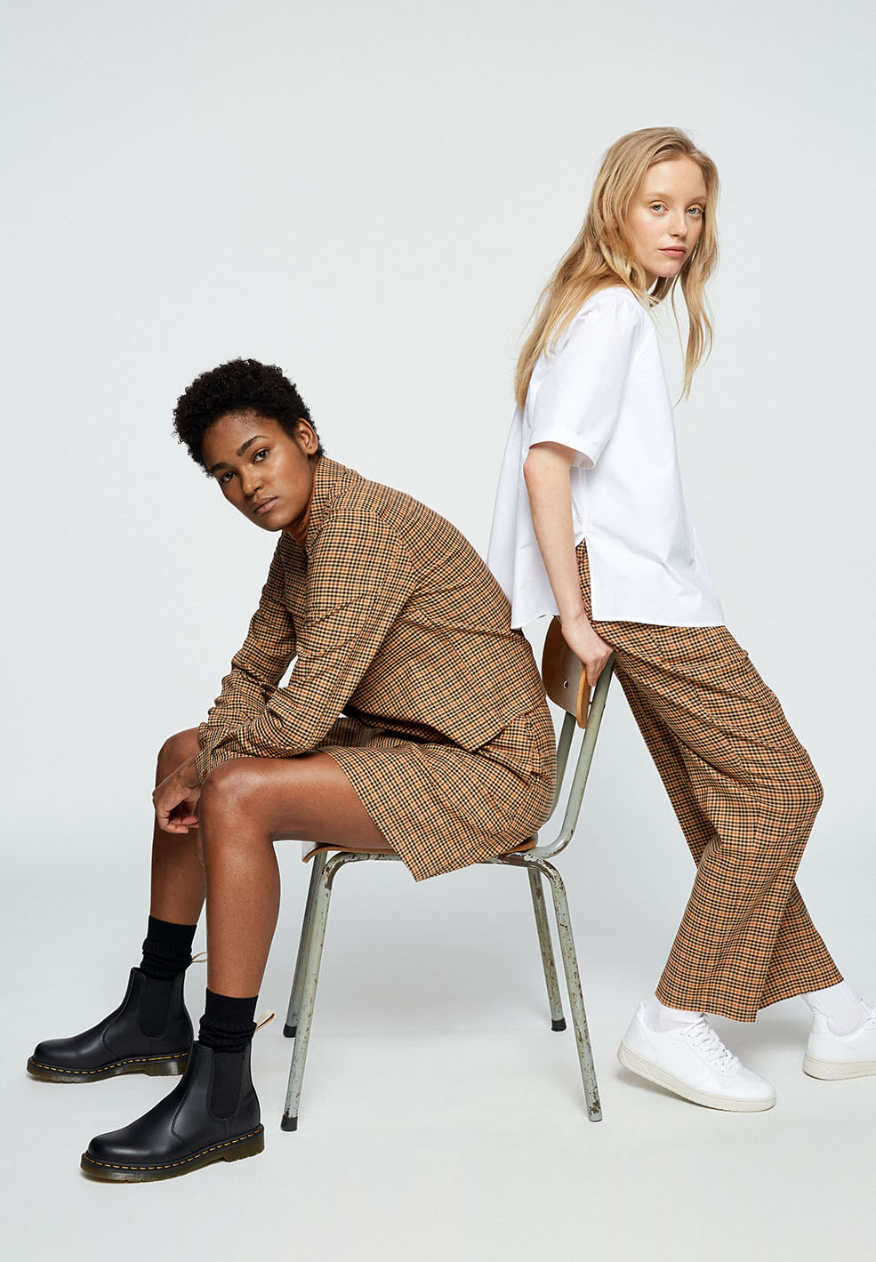 Two models wearing gold printed shorts, long sleeve shirt and pants and a white T-shirt from sustainable brand Armedangels with black and white shoes