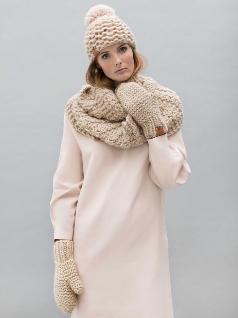 Model wearing a pink longsleeve dress with a beige scarf, hat and mittens from Granny's Finest