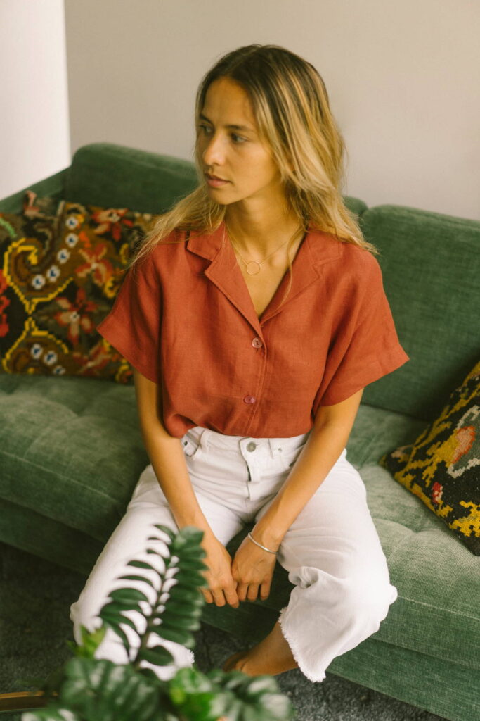 Model wearing red short sleeve button-up shirt and white pants from Hopaal while sitting on a green sofa