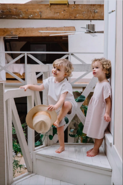 Two children wearing a white T-shirt and grey shorts and a pink dress from sustainable brand Studio Boheme