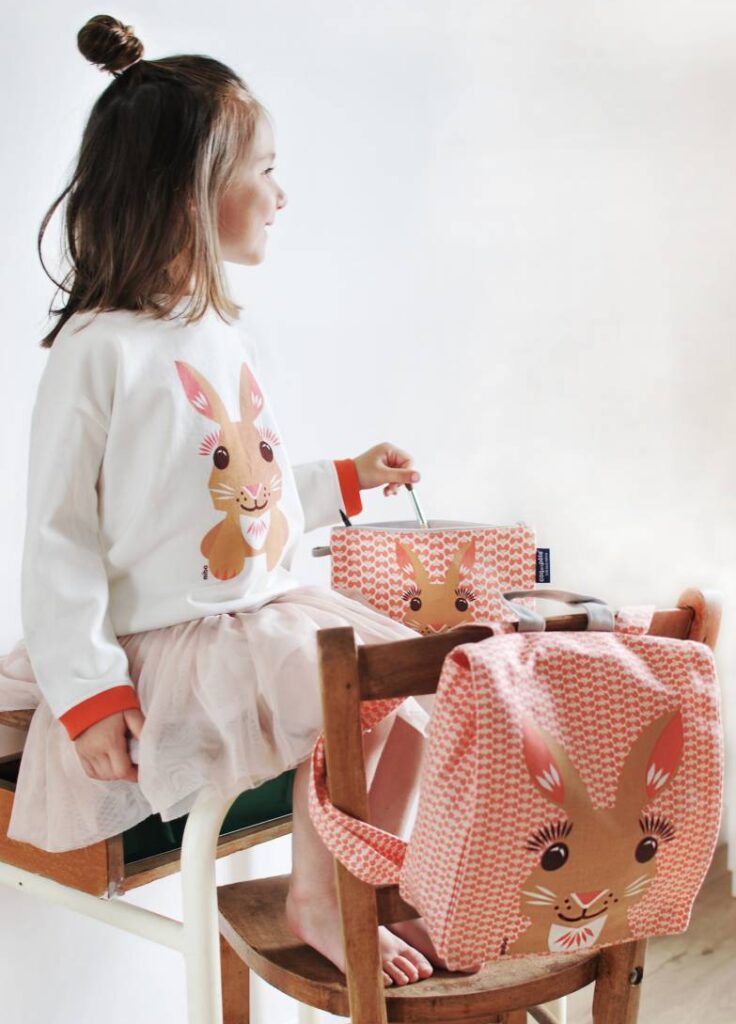 A girl wearing a white sweater with a bunny on it and a pink tule skirt and a pink printed backpack with a bunny on it from coq en pate