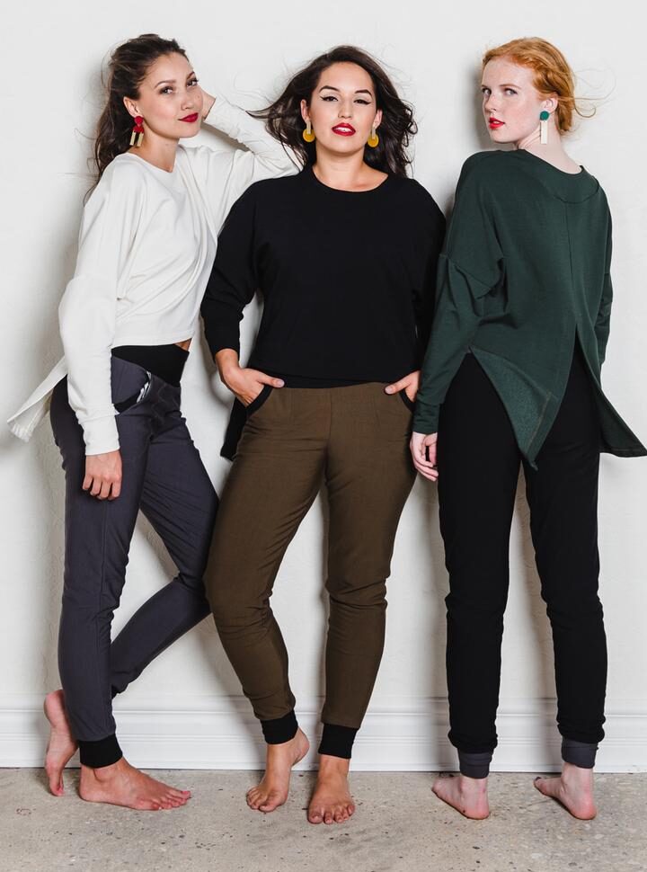 Three models wearing black, grey and brown pants and white, black and green tops from Anne Mulaire