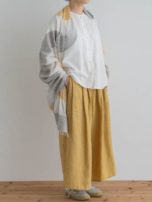 Model wearing a white top and a grey and white scarf and yellow wide pants from MAITO