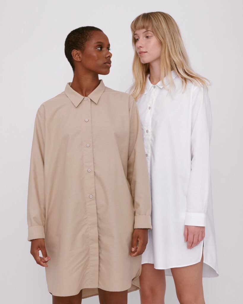 Two models wearing long button-up shirts in beige and white from Organic Basics
