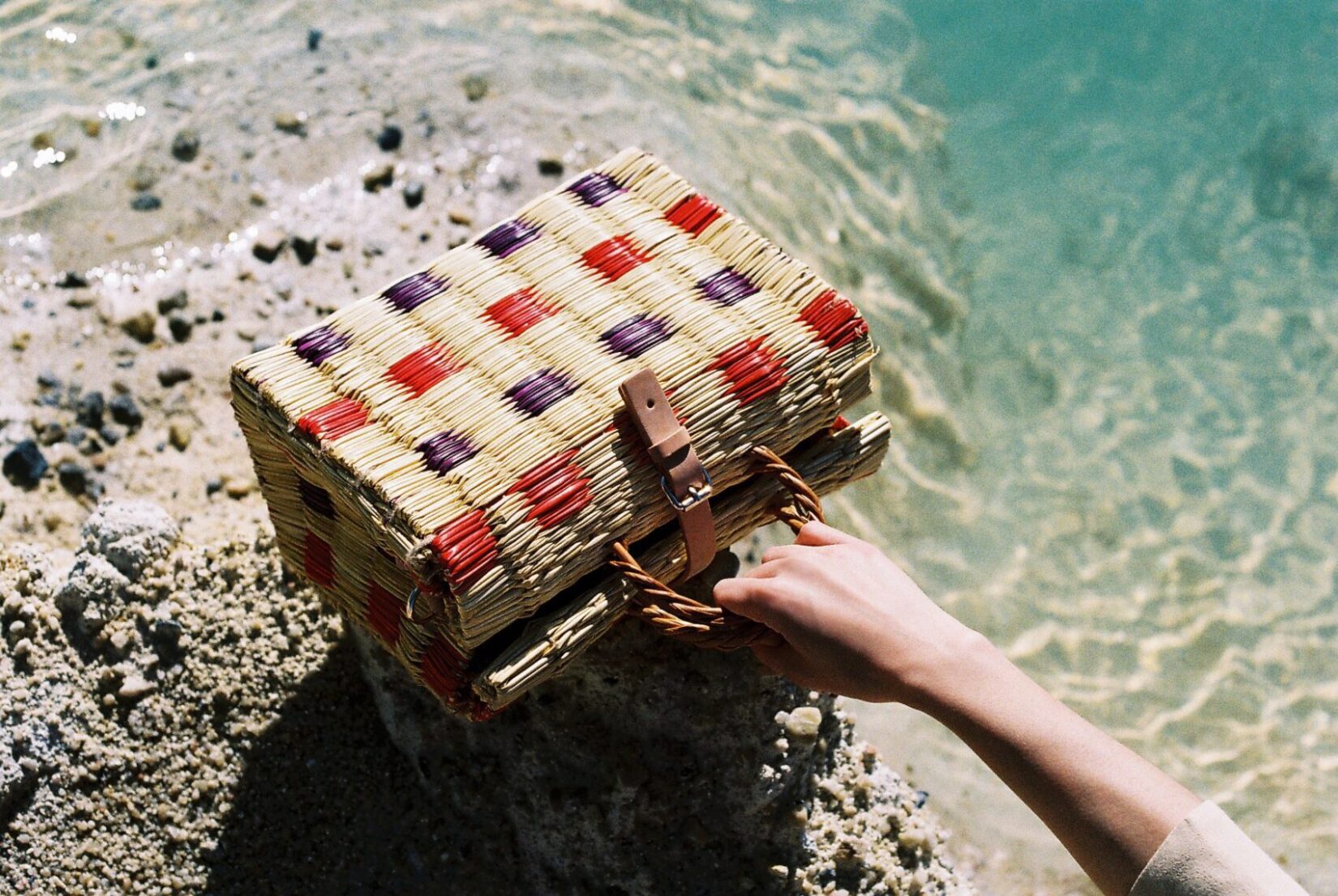 Straw bag with red and purple colours from TOINO ABEL photographed at the beach
