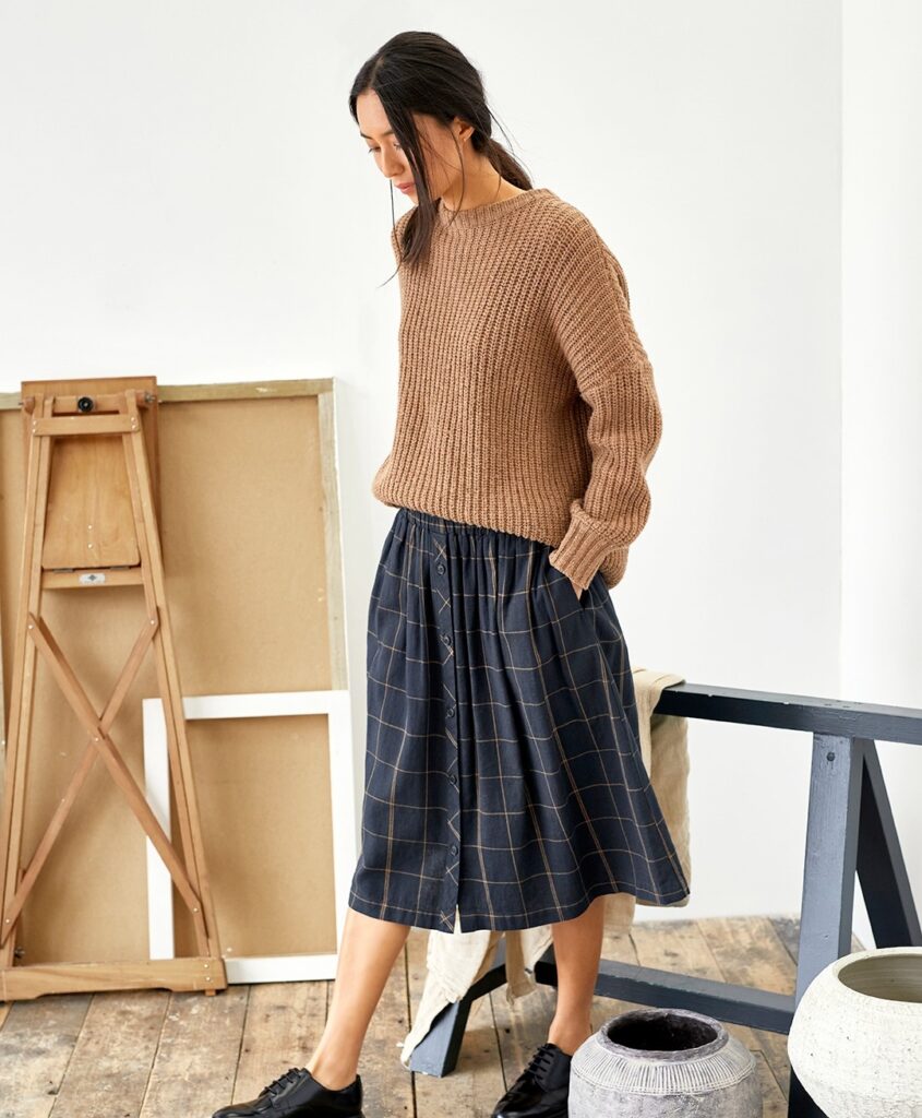 Model wearing a midi checked dark blue skirt with a beige sweater from Thought