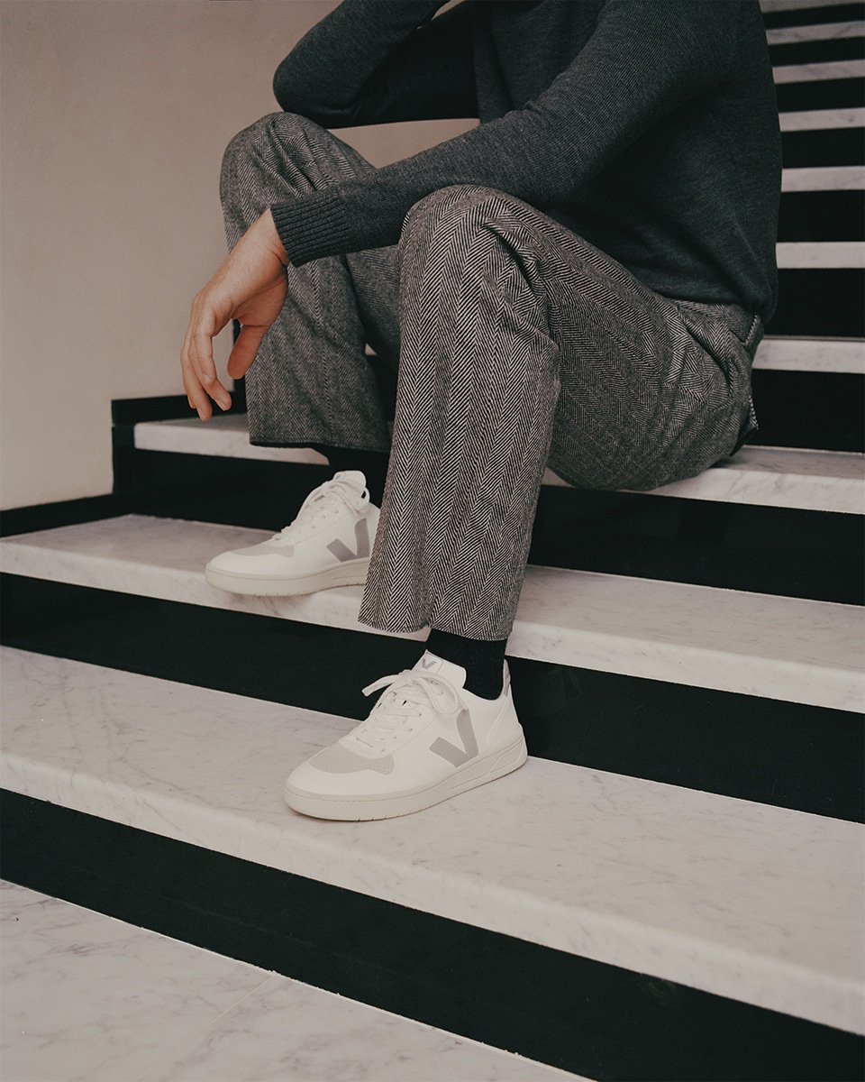 Model wearing grey pants and a dark grey sweater and white and off-white sneakers from VEJA
