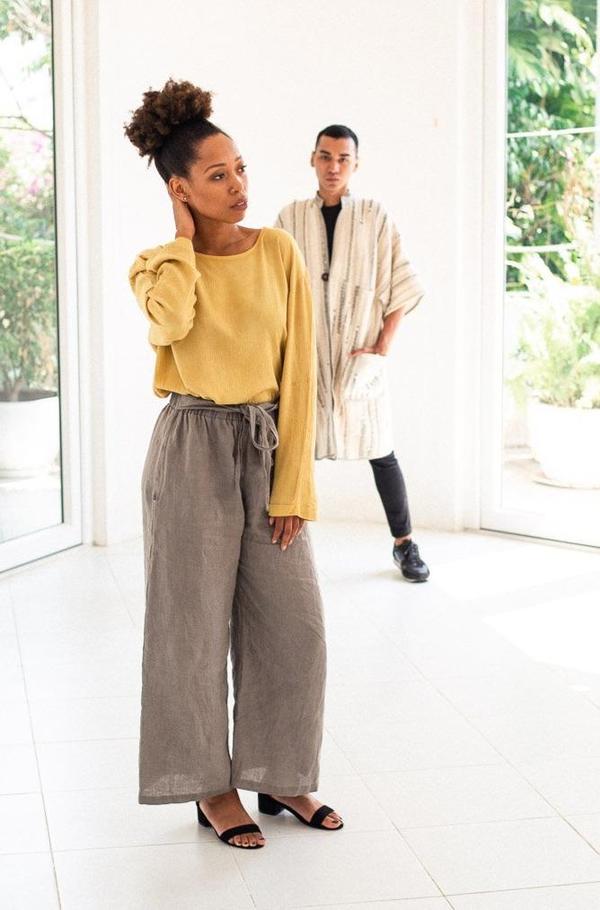 Male and female model wearing brown wide pants with a yellow sweater and a long beige kimono style jacket and black pants and a top from Tonlé
