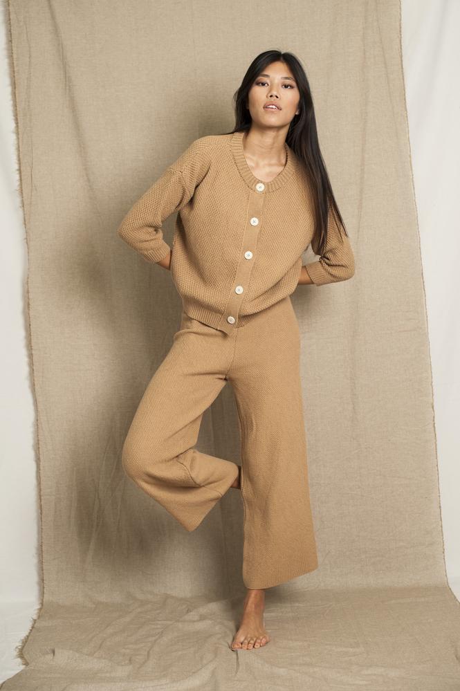 Model wearing beige knitted loose pants with a matching cardigan photographed in front of a beige background