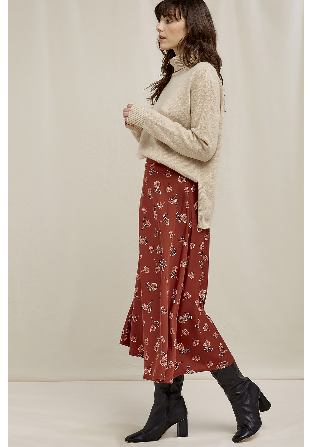 Model wearing a long red printed skirt with a beige turtleneck sweater from People Tree with black heeled boots
