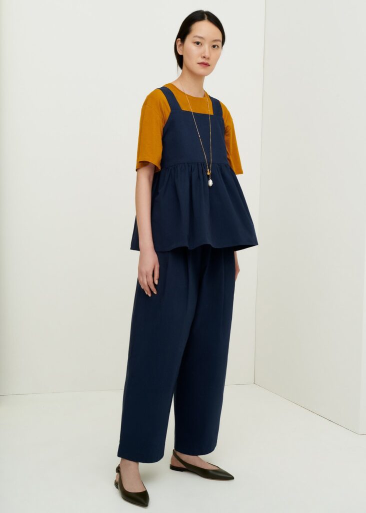 Model wearing dark blue wide trousers, a dark blue peplum top and an orange T-shirt from Kowtow with black shoes and a long necklace