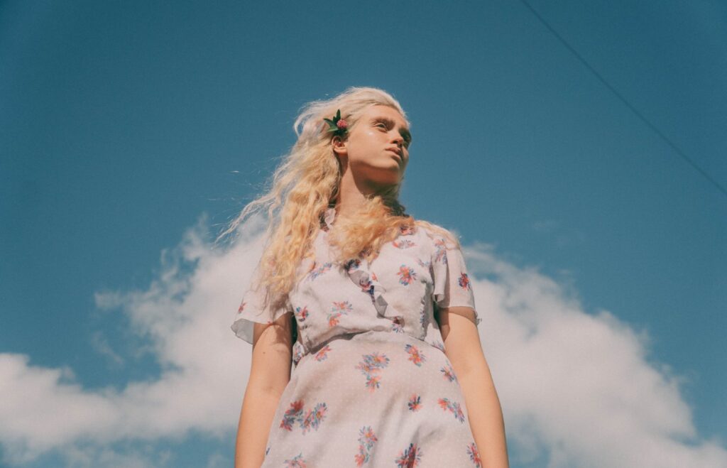 Thumbnail for article 'REDUCE & REUSE: Swap Your Dress'. Model wearing a white floral dress with a blue sky and clouds in the background