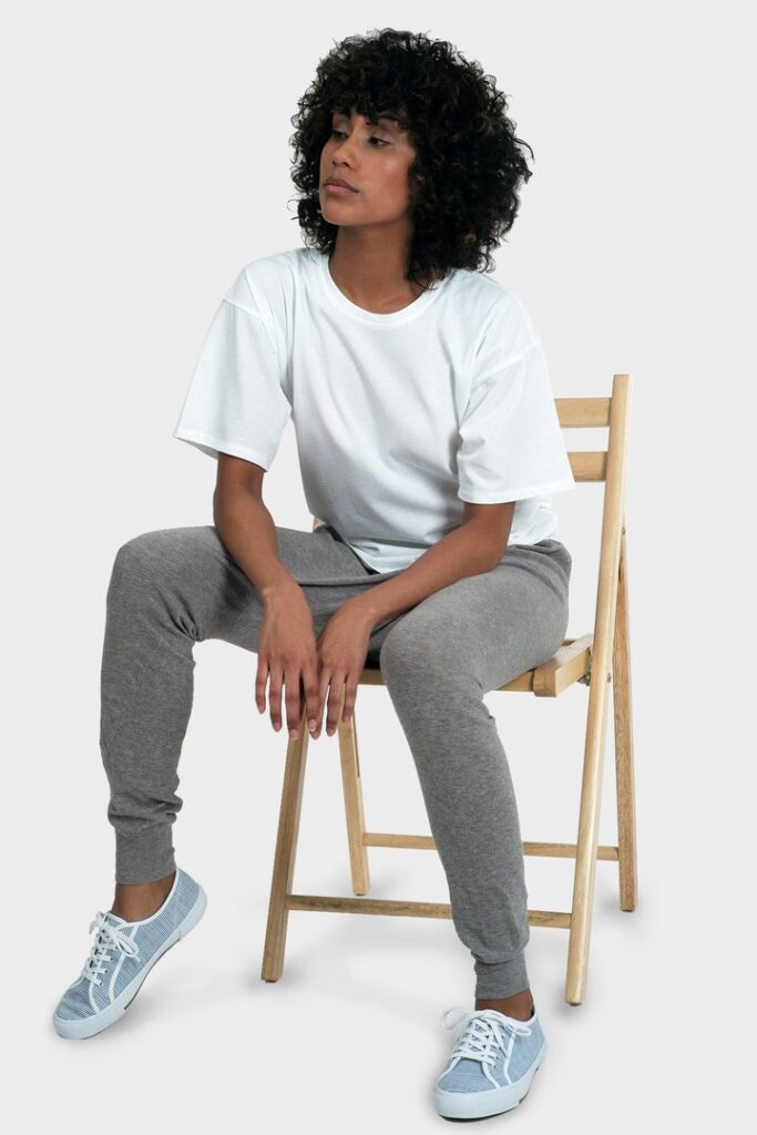 Model wearing grey sweatpants and a white T-shirt from 337 BRAND with light blue sneakers while sitting on a chair