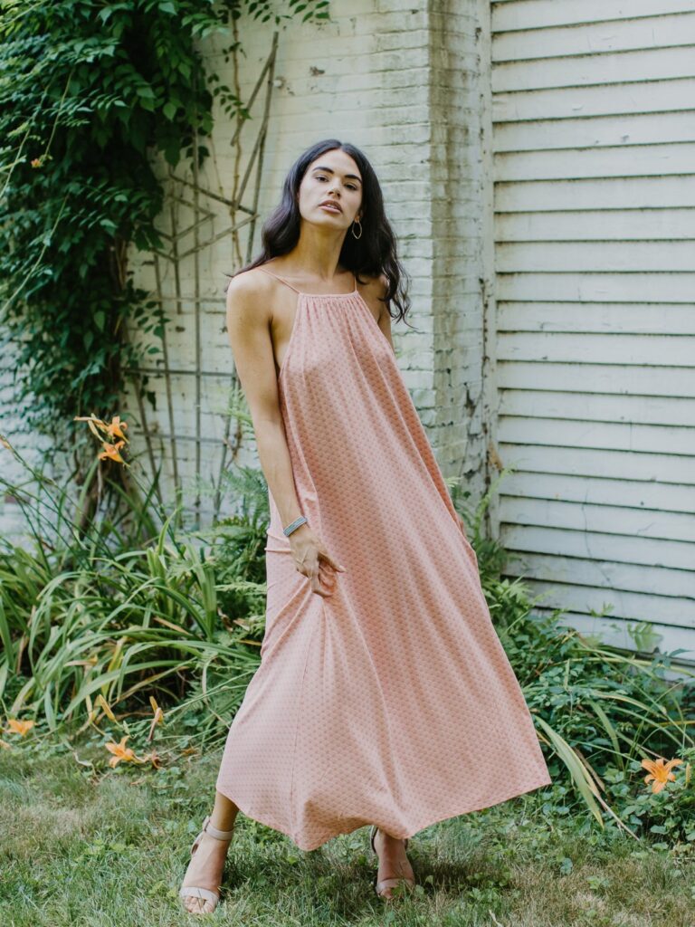 Model wearing a light pink maxi dress from Ash & Rose in front of a white wall outside
