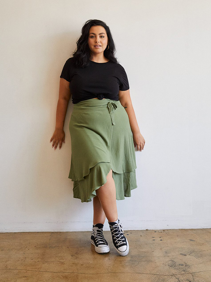 Plus size model wearing a green midi wrap skirt and a black T-shirt from For Days with black sneakers