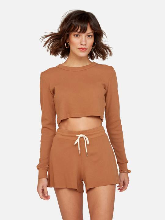 Model wearing copper coloured sweat shorts and a matching cropped sweater from sustainable brand MATE