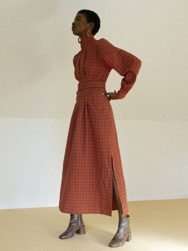 Model wearing a red maxi dress with a checkered pattern and wide sleeves, with grey ankle boots from sustainable brand Consciously