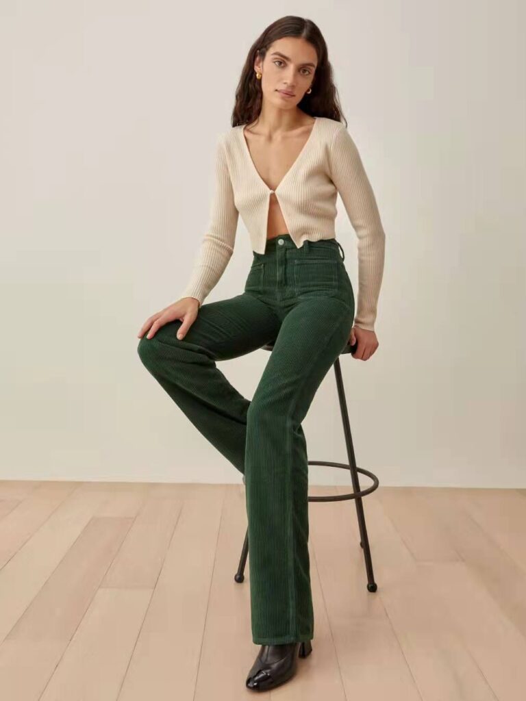 Model wearing dark green straight leg pants with a beige cropped cardigan from sustainable brand Reformation