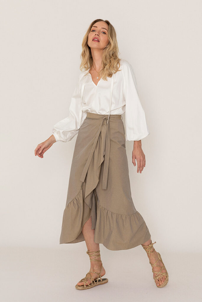 Model wearing a beige midi length wrap skirt with a white blouse from sustainable brand Hupit