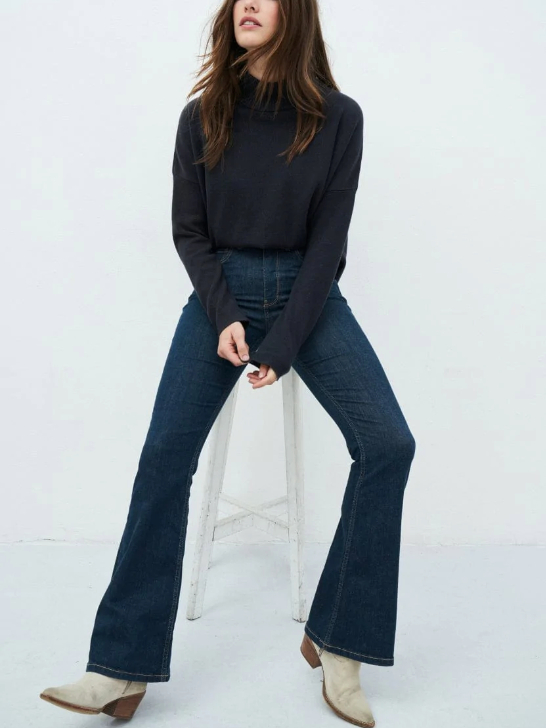 Model wearing dark blue flared jeans and a dark blue sweater from sustainable brand Kuyichi