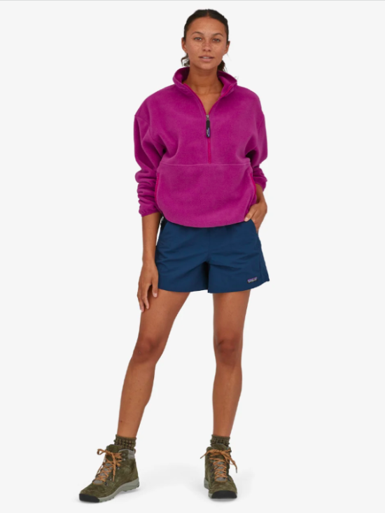 Model wearing a bright pink fleece top with dark blue shorts from Patagonia and boots