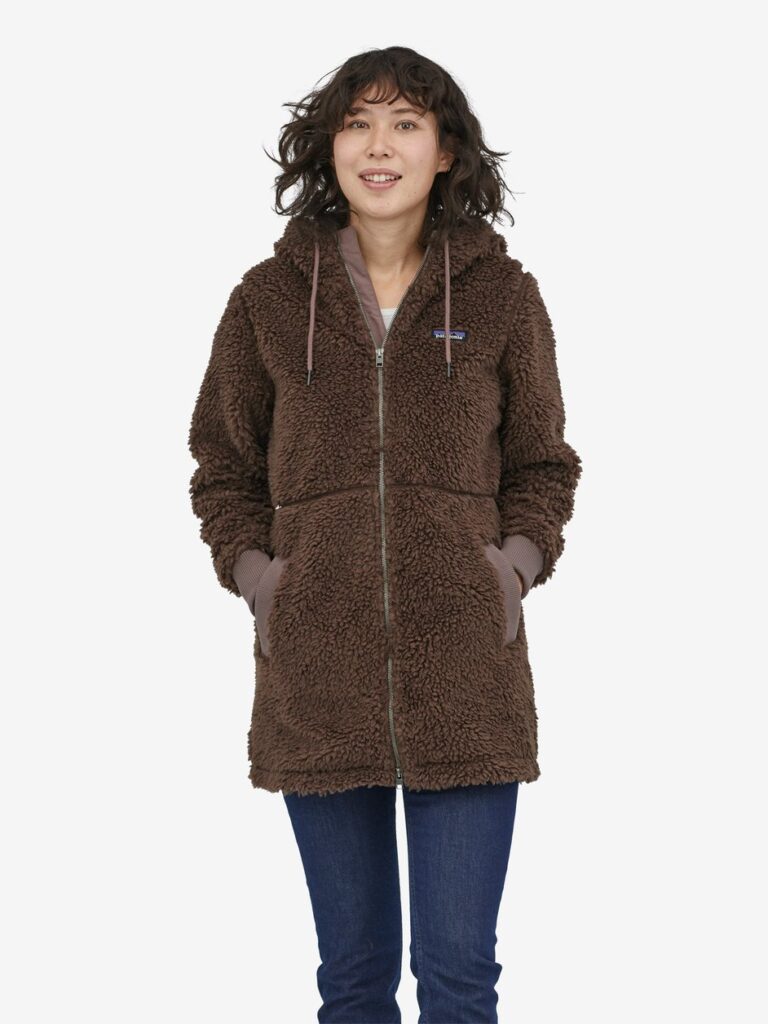 Model wearing a long brown teddy/fleece coat from Patagonia with blue pants