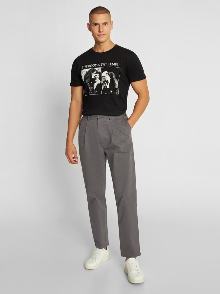 Male model wearing grey trousers with black graphic T-shirt from Dedicated