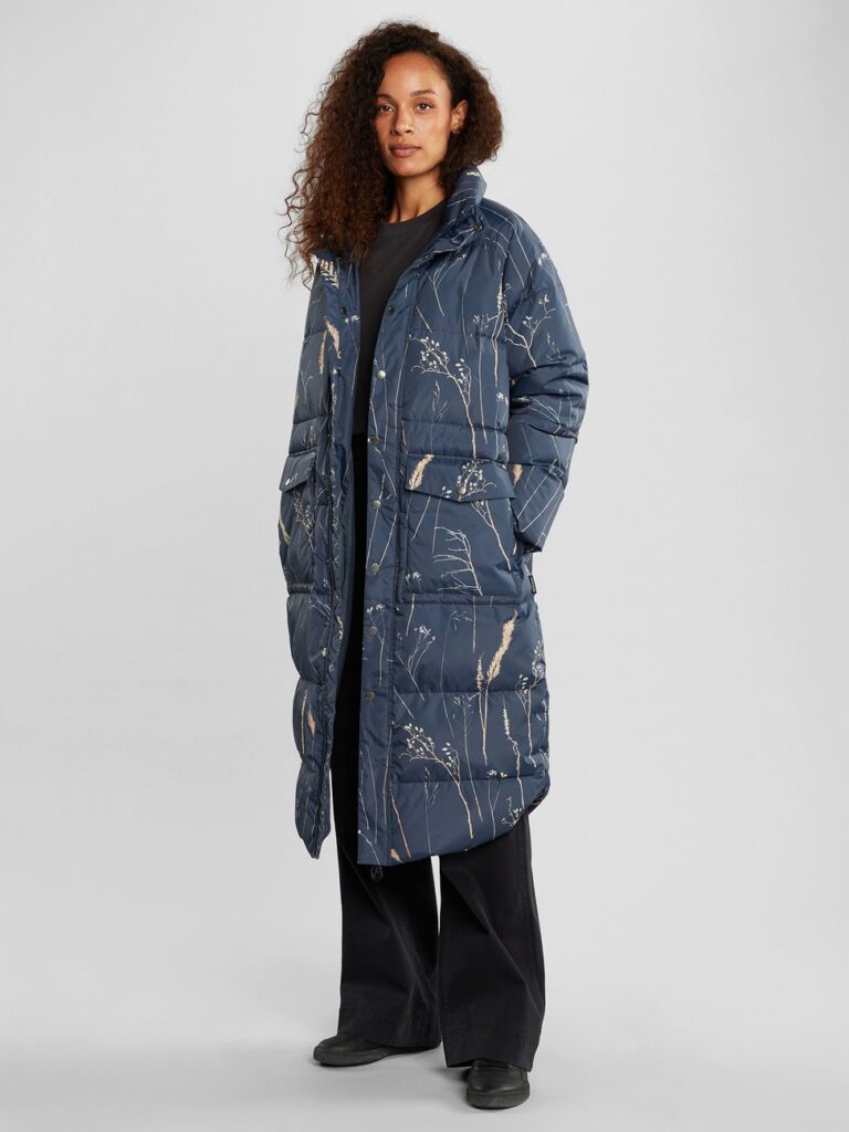 Model wearing long blue puffer jacket with plant print, with black pants from Dedicated