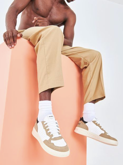 Male model wearing white and beige sneakers from sustainable brand Womsh