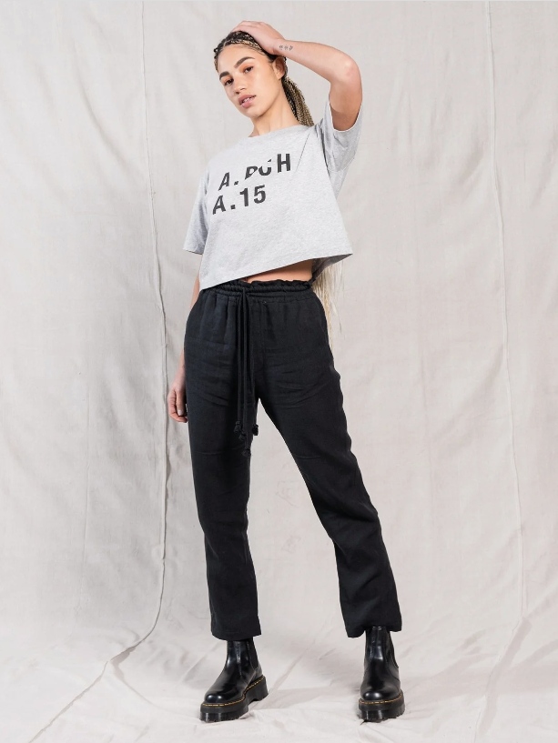 Female model wearing black pants, black boots and a grey cropped T-shirt with text on it from A.BCH
