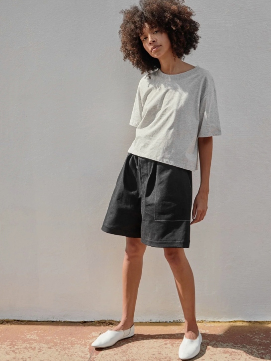 Female model wearing dark coloured wide shorts and a grey T-shirt from A.BCH with white shoes