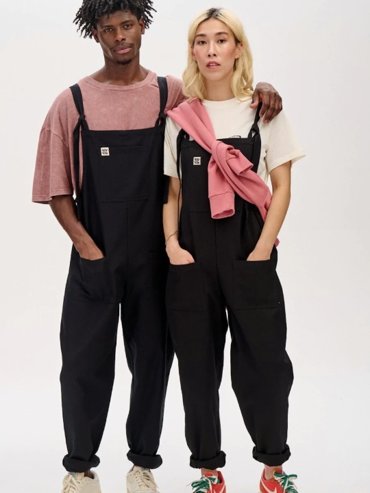 Male and female model wearing black dungarees with a white T-shirt and pink T-shirt from sustainable brand Lucy & Yak
