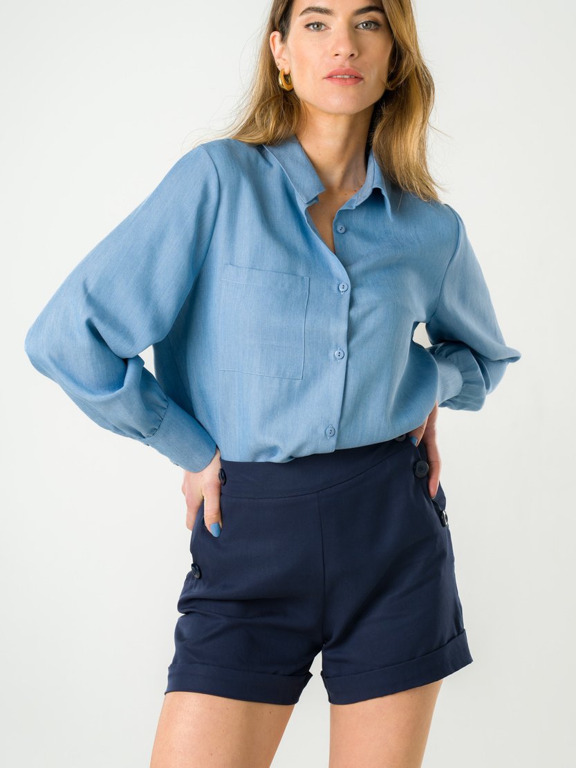 Model wearing a blue button-up shirt and dark blue shorts from sustainable brand Avani