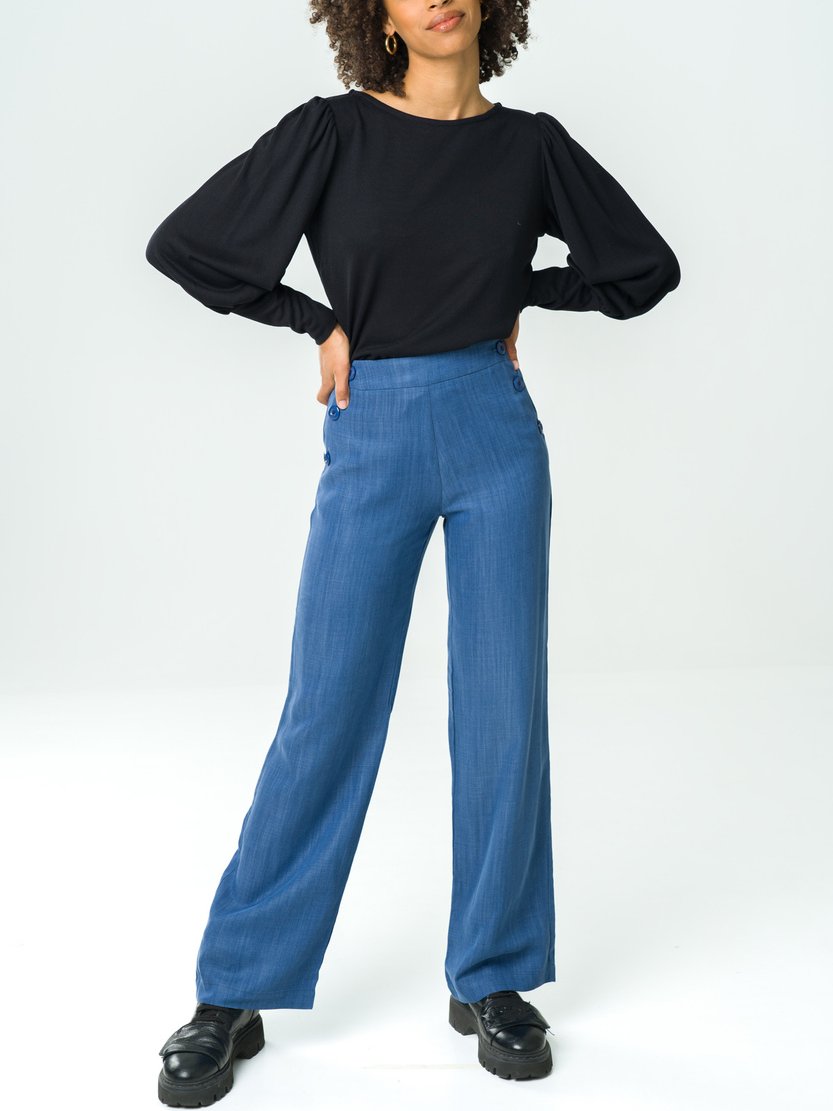 Model wearing a black long sleeve top and blue straight leg pants from sustainable brand Avani