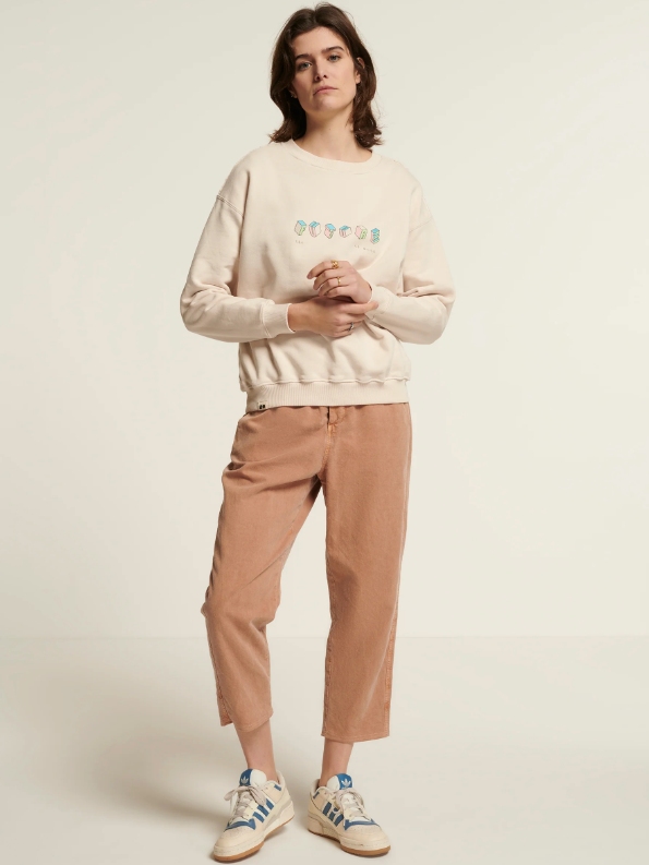Model wearing beige cropped pants and a beige/off-white sweatshirt from sustainable brand New Optimist