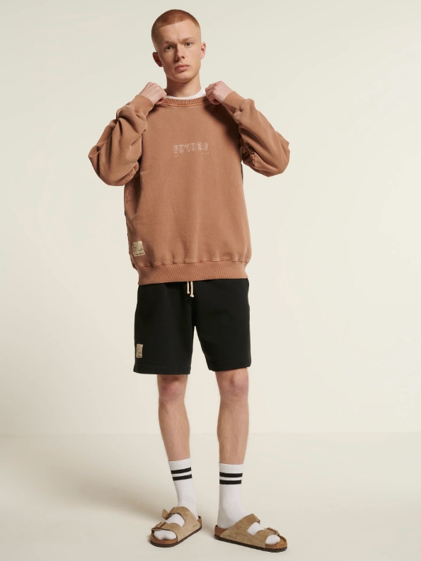 Male model wearing black shorts and a beige sweatshirt from sustainable brand New Optimist