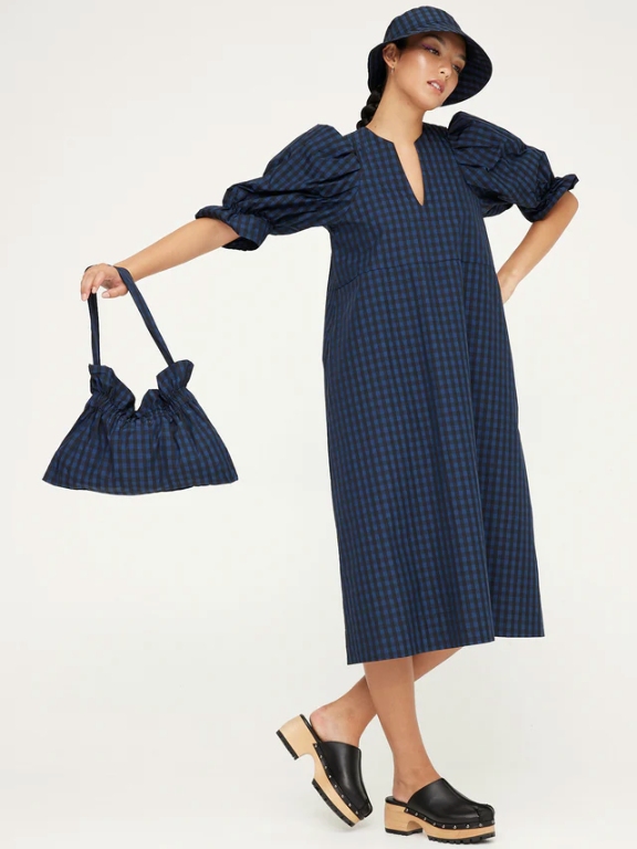 Model wearing a blue and black checkered midi length dress with puff sleeves, a matching bucket hat and a matching bag from sustainable brand Kuwaii