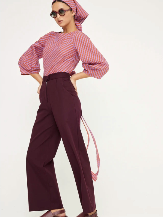 Model wearing burgundy wide leg trousers, a pink and orange checkered top and a matching head scarf from sustainable brand Kuwaii