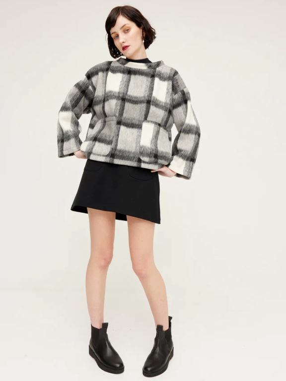 Model wearing a black mini skirt and a grey plaid sweater from sustainable brand Kuwaii