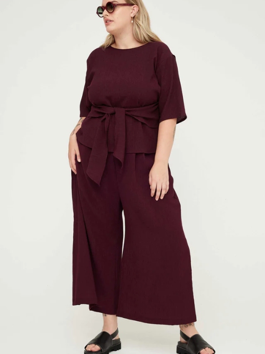 Model wearing burgundy wide leg pants and a burgundy short sleeve top from sustainable brand Kuwaii