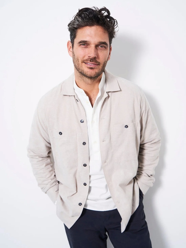 Male model wearing dark blue pants, a white button-up shirt and a beige overshirt from sustainable brand NEEM