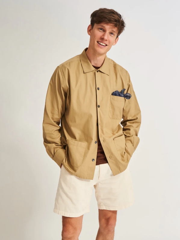 Male model wearing off-white shorts, a brown T-shirt and a beige overshirt from sustainable brand NEEM