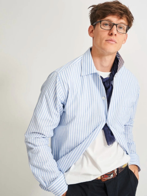 Male model wearing black pants, a white T-shirt, a blue and white striped button-up shirt and a blue scarf from sustainable brand NEEM