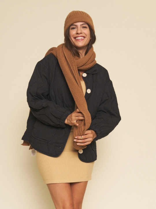 Model wearing a beige tight mini dress, a black padded jacket, a brown scarf and a brown beanie from sustainable brand Whimsy + Row